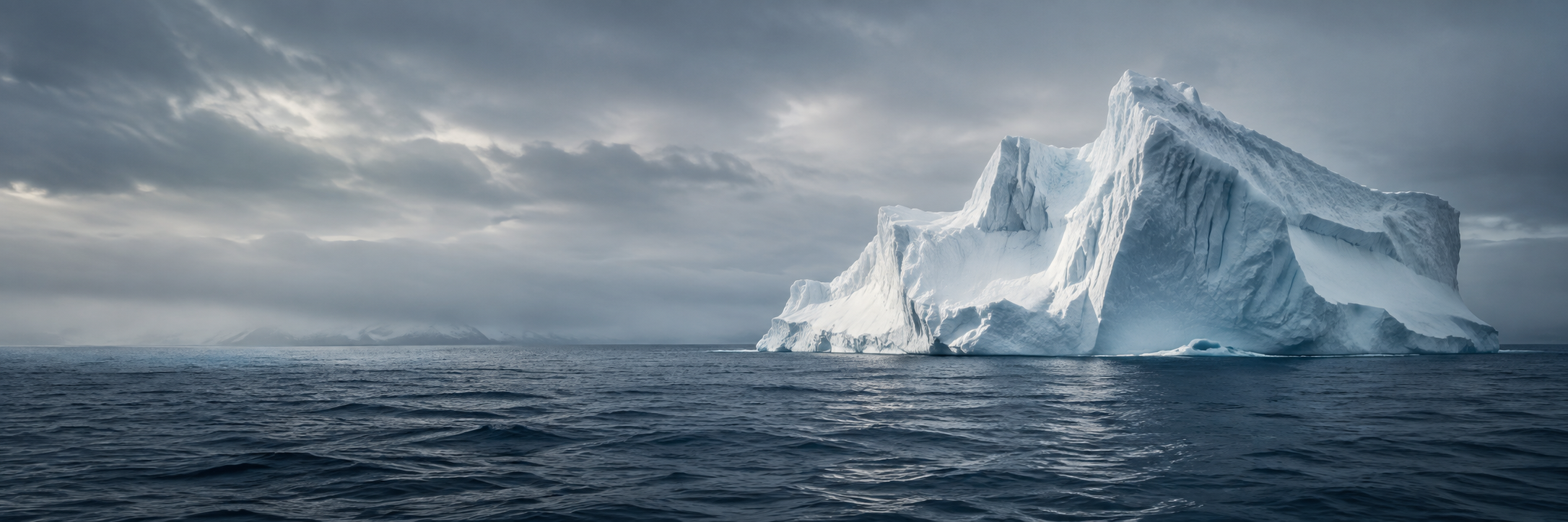 A blue-white iceberg rising above a calm, dark sea